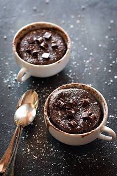 two mugs filled with chocolate pudding on top of a black table next to spoons