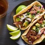 three tacos on a plate with limes and beer