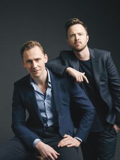 two men sitting next to each other in front of a black background and one is pointing at the camera