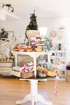 a white table topped with lots of boxes and baskets next to a small christmas tree