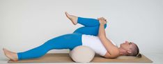 a woman in blue pants and white shirt is laying on a yoga mat