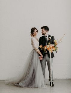 a man and woman standing next to each other in front of a white wall holding flowers