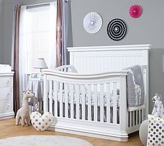 a white baby crib in a room with gray walls and polka dot pillows on the floor