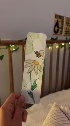 a person holding up a piece of paper with flowers on it in front of a bed