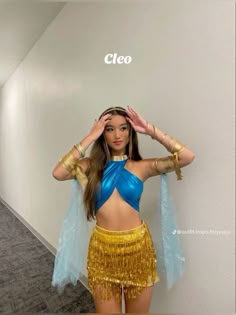 a woman in a blue top and gold skirt posing for the camera with her hands on her head