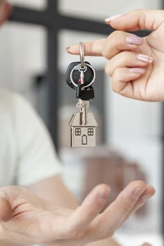 two hands holding keys to a house shaped keychain in front of a woman's hand