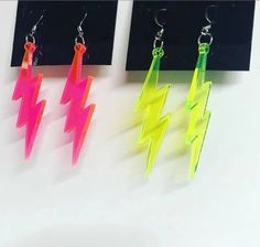 three pairs of neon colored lightning earrings hanging from hooks on a white surface with black background