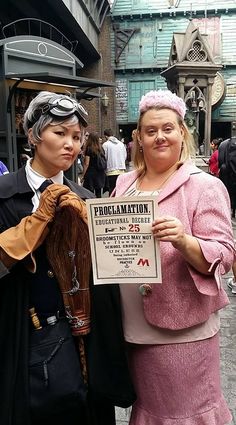 two women dressed in costumes standing next to each other on a street with people walking by