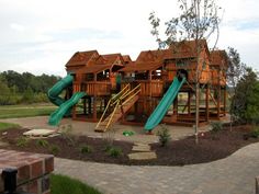 a large wooden play set with slides in the middle of a brick walkway next to trees and grass