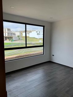 an empty room with wood flooring and large window overlooking the yard outside, in front of a white building