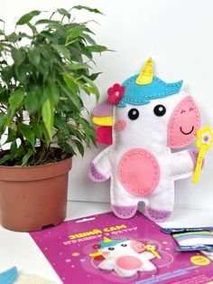 a stuffed unicorn toy next to a potted plant and book on a table with scissors