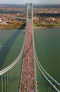 a large group of people walking across a bridge in the middle of the day,