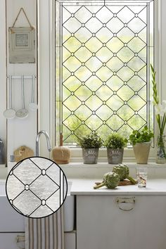 a kitchen window with potted plants on the counter and in front of it is a white cabinet