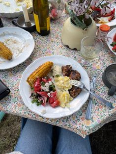 a person sitting at a table with plates of food in front of them, including corn on the cob and salad