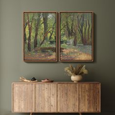 two paintings hang on the wall above a wooden cabinet in a room with green walls