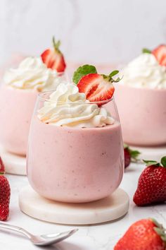 three desserts with strawberries and whipped cream in small glasses on a white table