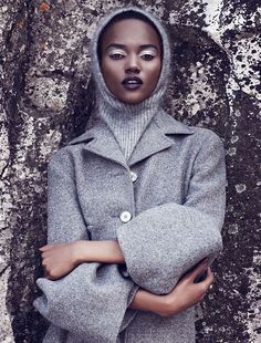 a woman in grey coat and hat standing next to a tree