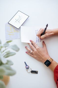 a woman's hands holding a pen and writing on top of a notepad