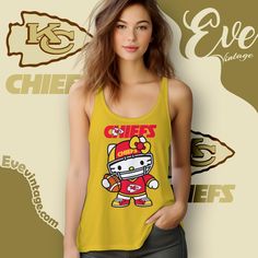 Kansas City Chiefs Hello Kitty Shirt The Kansas City Chiefs Hello Kitty Shirt is an adorable fusion of football and fun. This design showcases Hello Kitty dressed up in the Chiefs’ iconic red and yellow football gear, complete with a helmet and jersey featuring the team’s logo. It’s a perfect way to celebrate your love... Fan Apparel Tops With Character Print For Sports Events, Sporty Tops With Character Print For Sports Events, Game Day Yellow Graphic Print Tops, Sports Fan Apparel Tops With Character Print, Yellow Graphic Print Top For Game Day, Yellow Tops For Sports Events, Yellow Sports Tops With Team Name, Sporty Yellow Top Fan Merchandise, Hello Kitty Shirt