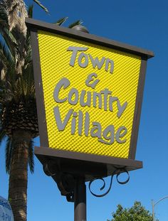 a yellow sign that says town and country village on it's side with palm trees in the background