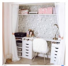 a white desk with drawers and shelves in front of a wallpapered wall behind it