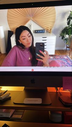 a woman is looking at her phone while sitting in front of the computer screen