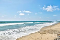 a sandy beach next to the ocean under a blue sky with white clouds and waves