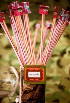 several red and white striped straws in a glass vase with wine glasses behind it