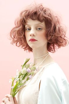 a woman with red hair holding flowers in her hand and looking off to the side