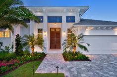 a white house with palm trees in front of it and landscaping around the entrance area