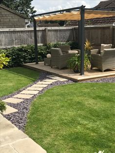 a patio with chairs and an umbrella in the grass next to a wooden decking area