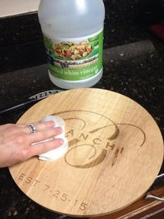 a person using a cloth to clean a wooden cutting board with a bottle of deodorant in the background