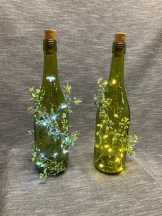 two green bottles with plants in them sitting on a gray cloth covered surface, one is lit up and the other is empty