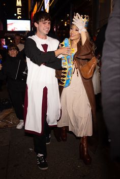 two people dressed in costumes are walking down the street at night, one is holding a candy bar