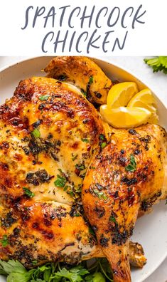 a white plate topped with chicken and garnished with parsley next to lemon wedges