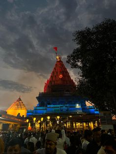 people are standing around in front of a temple at night with lights on the roof