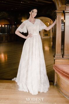 a woman in a white wedding dress standing on a wooden floor with her hands on her hips