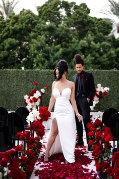 a man and woman standing next to each other in front of red roses on the ground