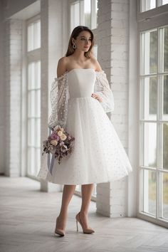 a woman wearing a white dress and holding a bouquet in front of an open window