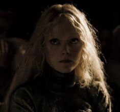 a woman with long blonde hair is staring at the camera in a dimly lit room