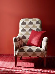 a chair sitting in front of a red wall with pillows on it's back