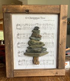 a christmas tree made out of rocks on top of sheet music in a wooden frame