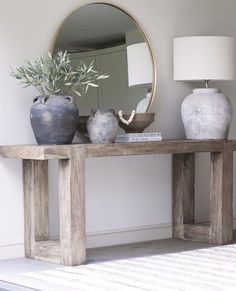 a table with two vases and a mirror on top of it next to a lamp