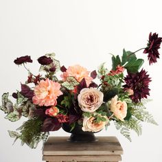 a vase filled with lots of flowers on top of a wooden table next to a white wall