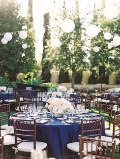 an outdoor wedding reception with blue table cloths and white centerpieces on the tables