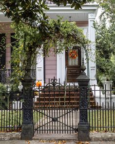 an iron gate is in front of a pink house with pumpkins on the porch