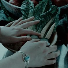 two hands reaching for some vegetables in a bowl