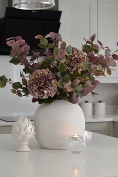 a vase filled with flowers sitting on top of a white countertop next to a candle