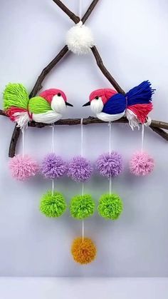 two colorful birds on a branch with pom - poms hanging from it's sides