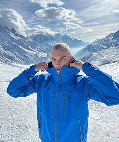 a man standing in the snow with his hands on his ears and wearing a blue jacket